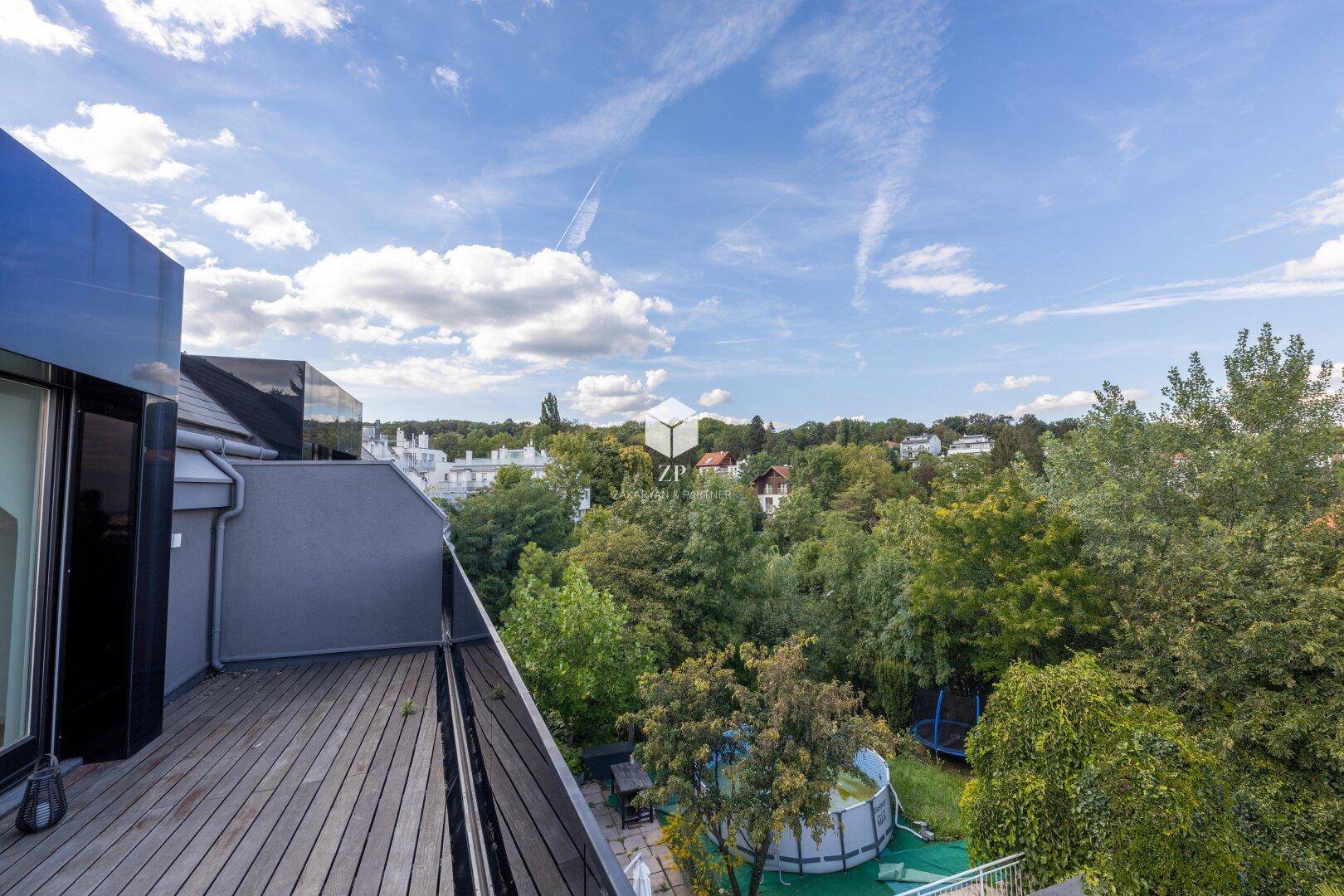 Balkon mit Holzboden und Glasgeländer, bietet Blick auf einen Pool und Bäume.