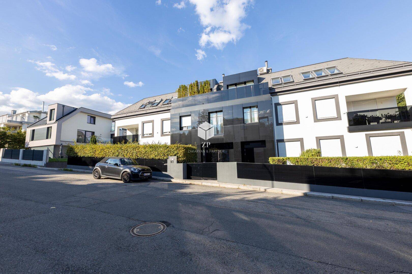 Moderne Wohnanlage mit dunkler Fassade, großen Fenstern und gepflegter Außenanlage.
