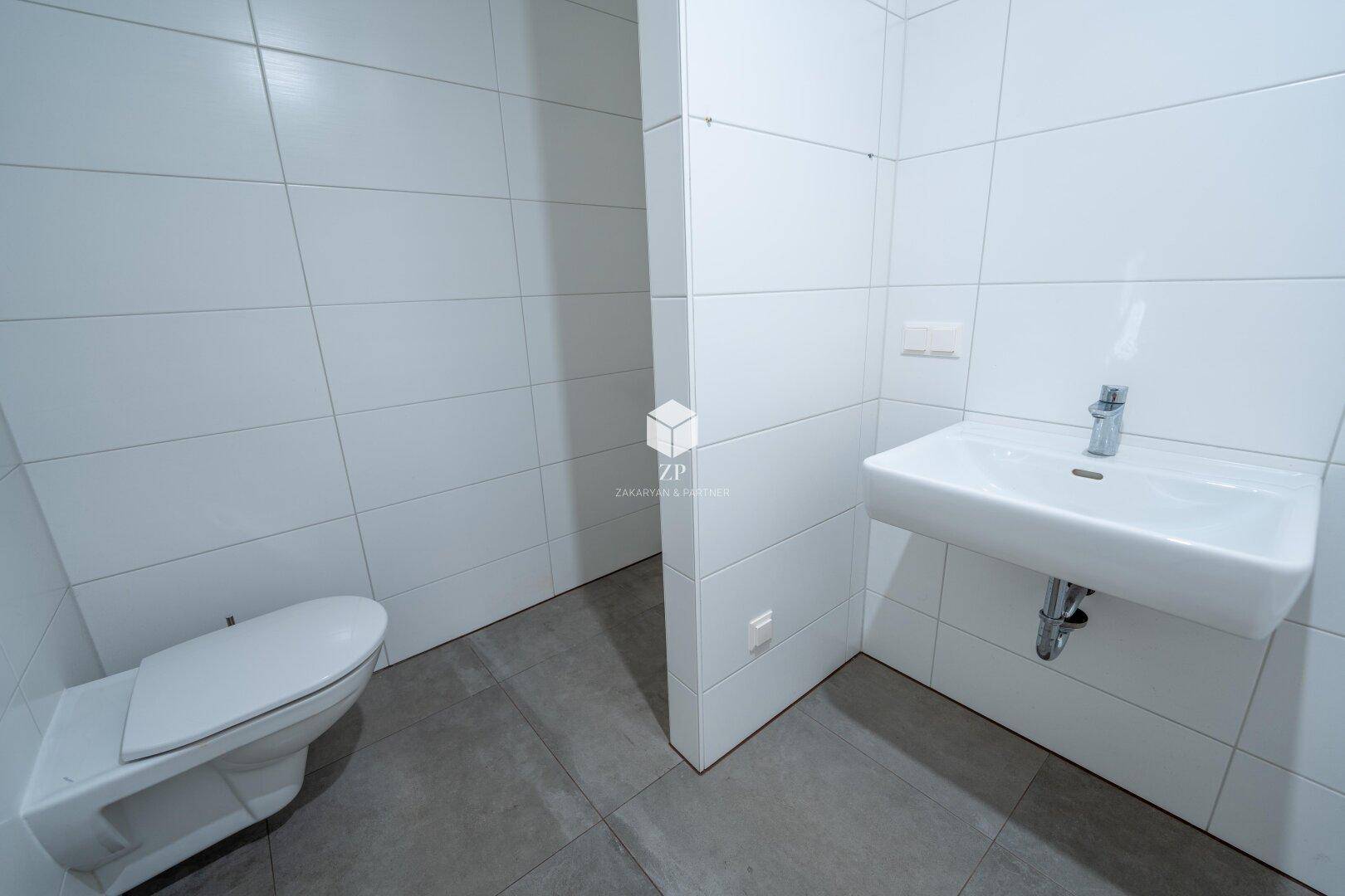 Modernes Gäste-WC mit weißen Fliesen, wandhängendem WC und kleinem Waschbecken.