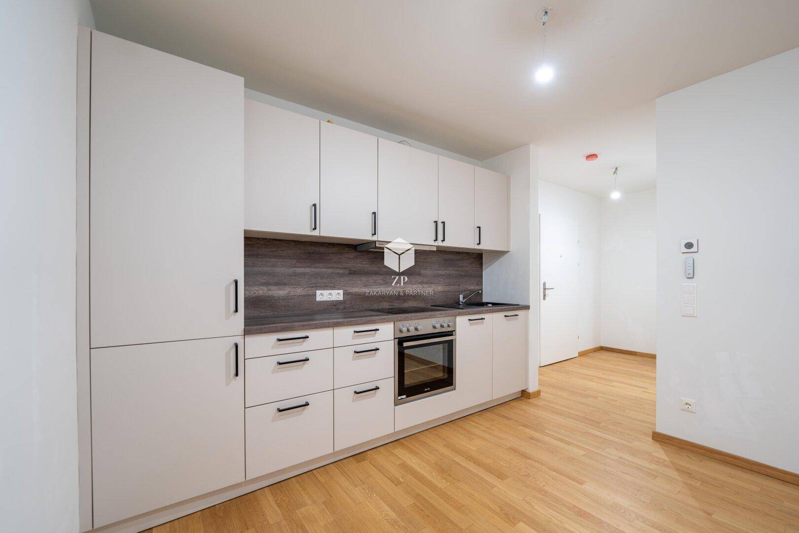 Nahaufnahme einer modernen Einbauküche mit weißen Schränken, dunkler Arbeitsplatte und Holzboden.