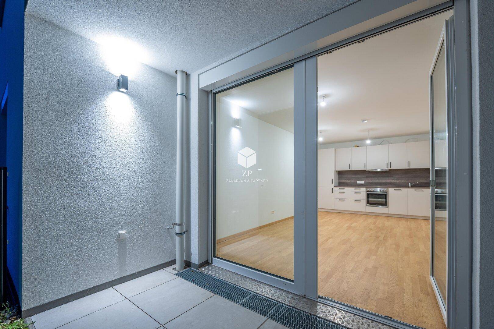Gemütliche Terrasse am Abend mit Außenbeleuchtung und Blick in den Innenraum der Wohnung.