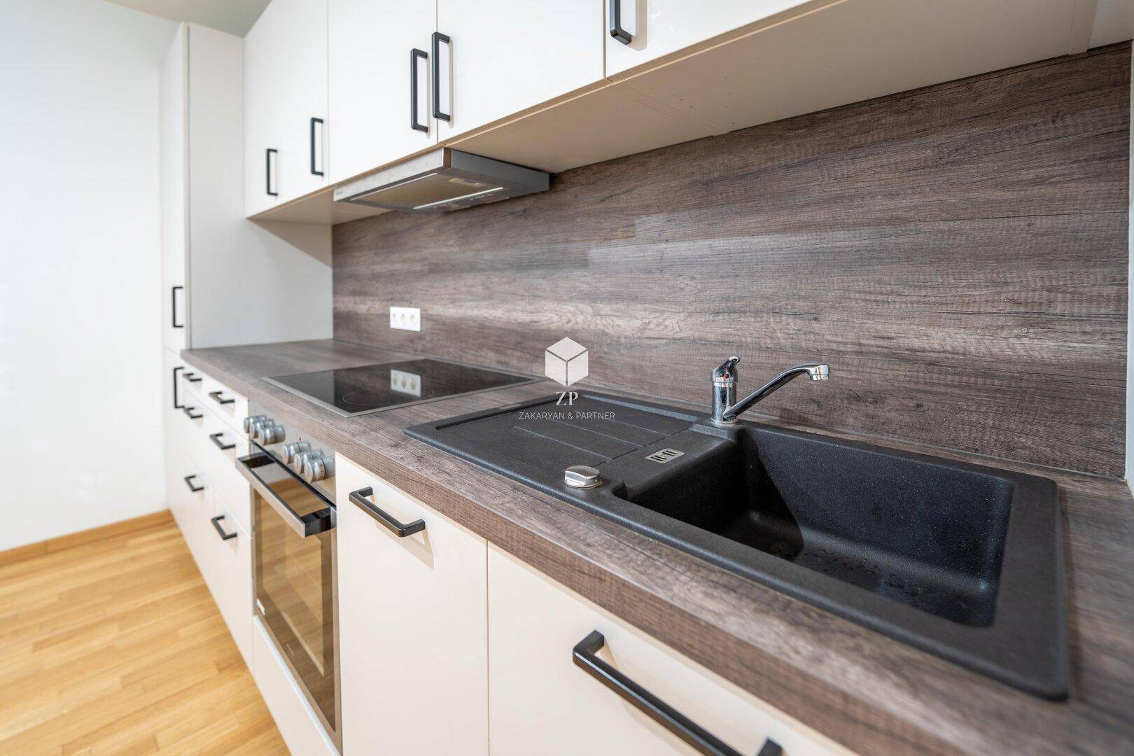 Detailansicht der Küchenzeile mit Spüle, Induktionskochfeld und Backofen in einer modernen Küche.