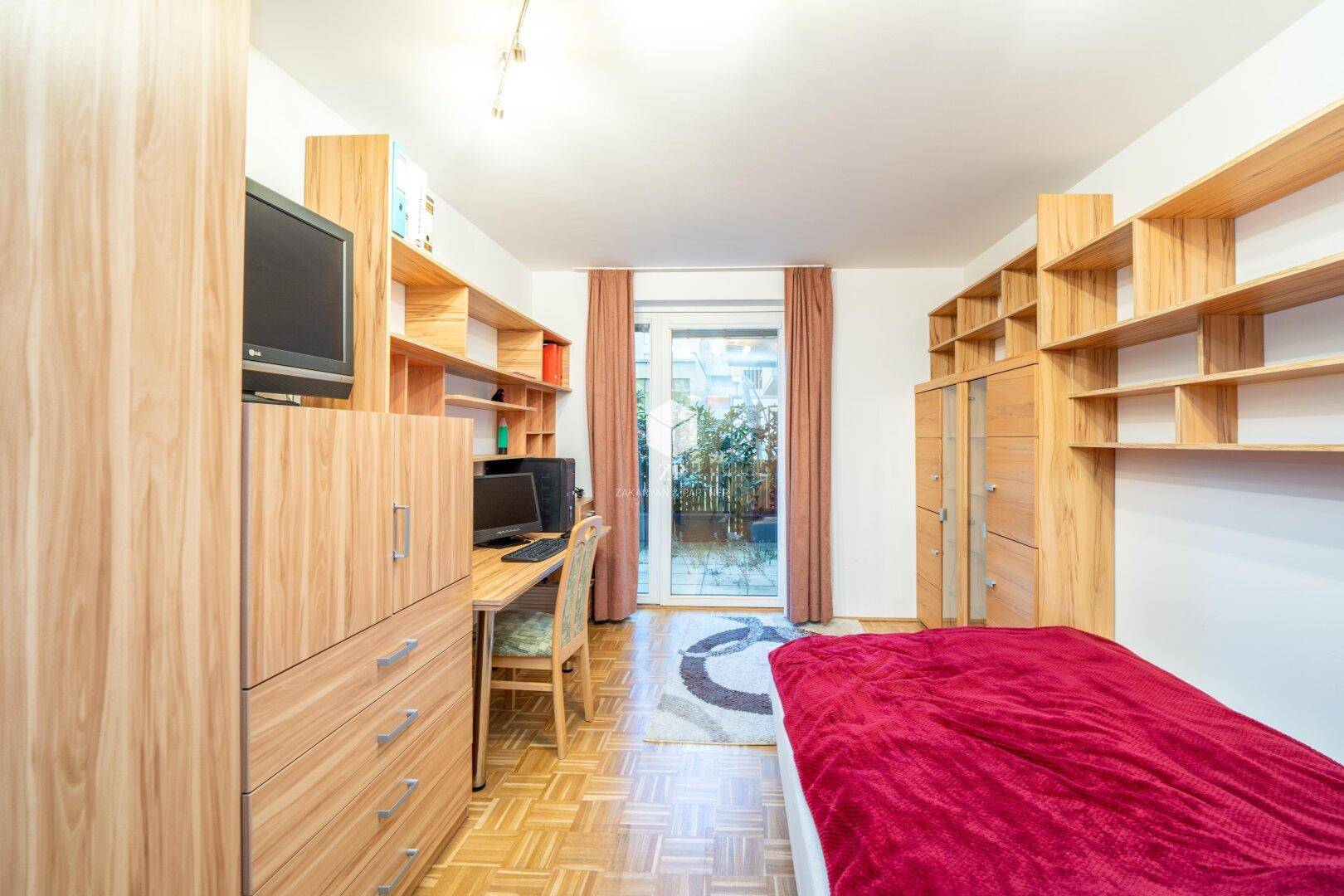 Schlafzimmer mit Parkettboden, Holzregalen und Zugang zum Balkon.