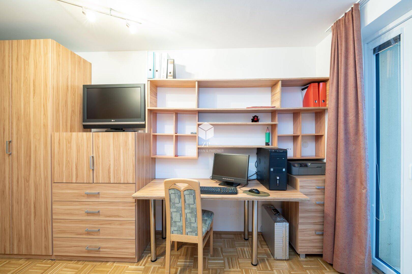 Arbeitsbereich mit Schreibtisch, Computer und Holzregalen.