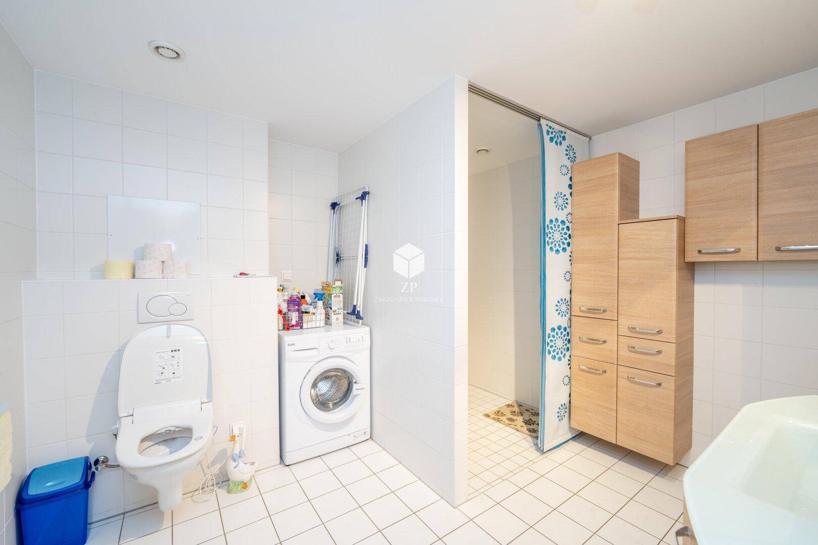 Badezimmer mit WC, Waschmaschine und Duschbereich.