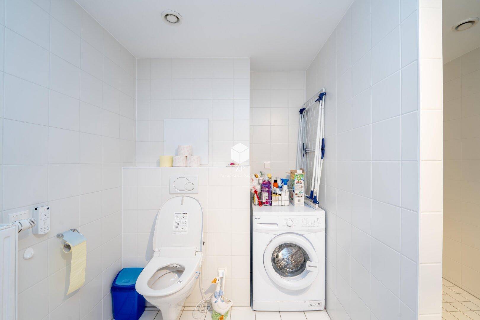 Badezimmer mit weiß gefliesten Wänden, WC und Waschmaschine.