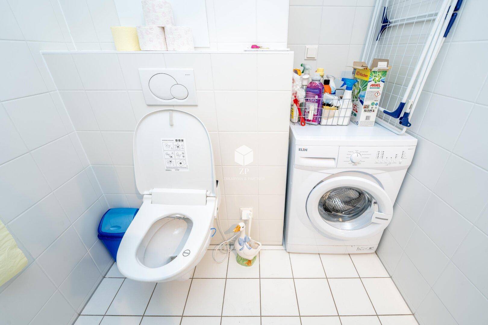WC-Bereich im Badezimmer mit Waschmaschine und Fliesenboden.