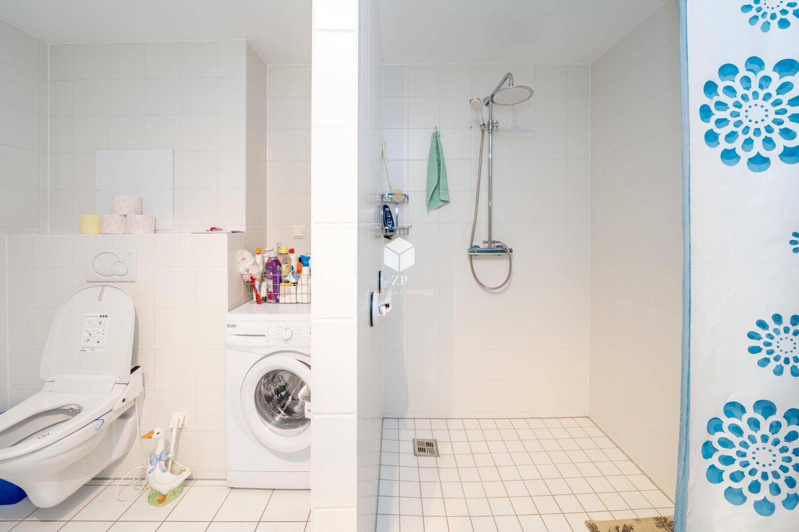 Badezimmer mit WC, Waschmaschine und begehbarer Dusche.