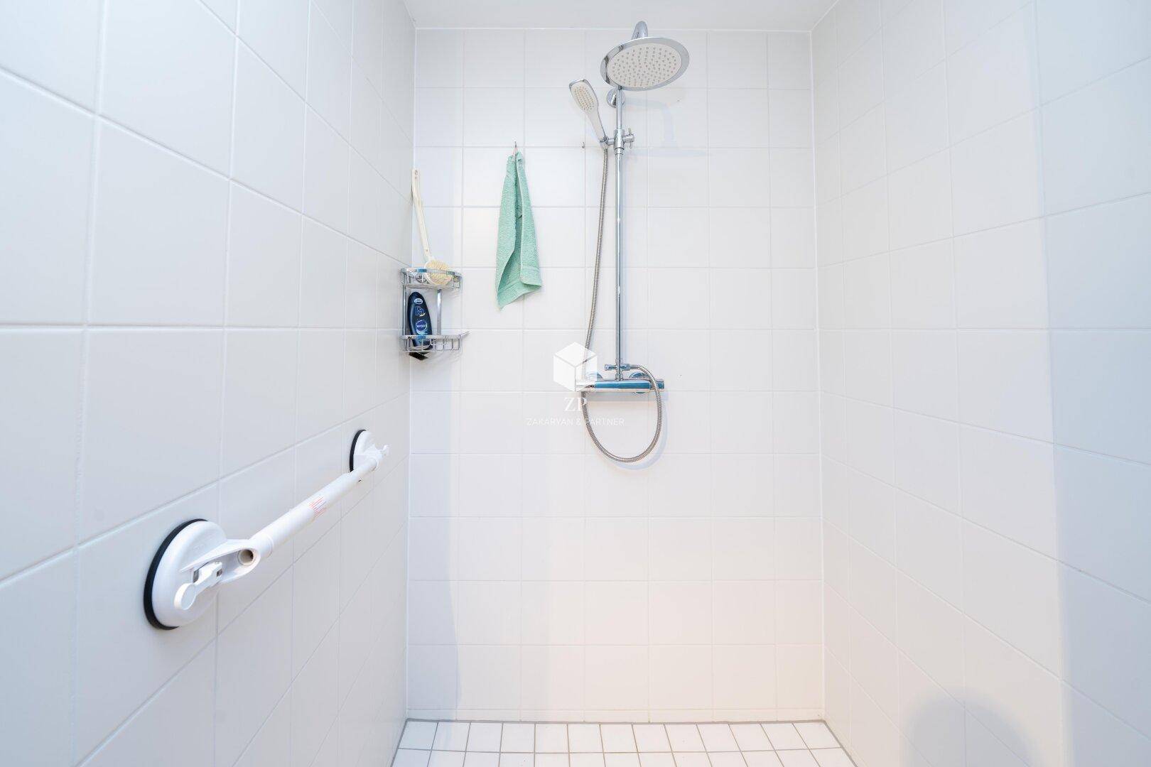 Duschbereich mit Regendusche und Haltegriff für zusätzliche Sicherheit.