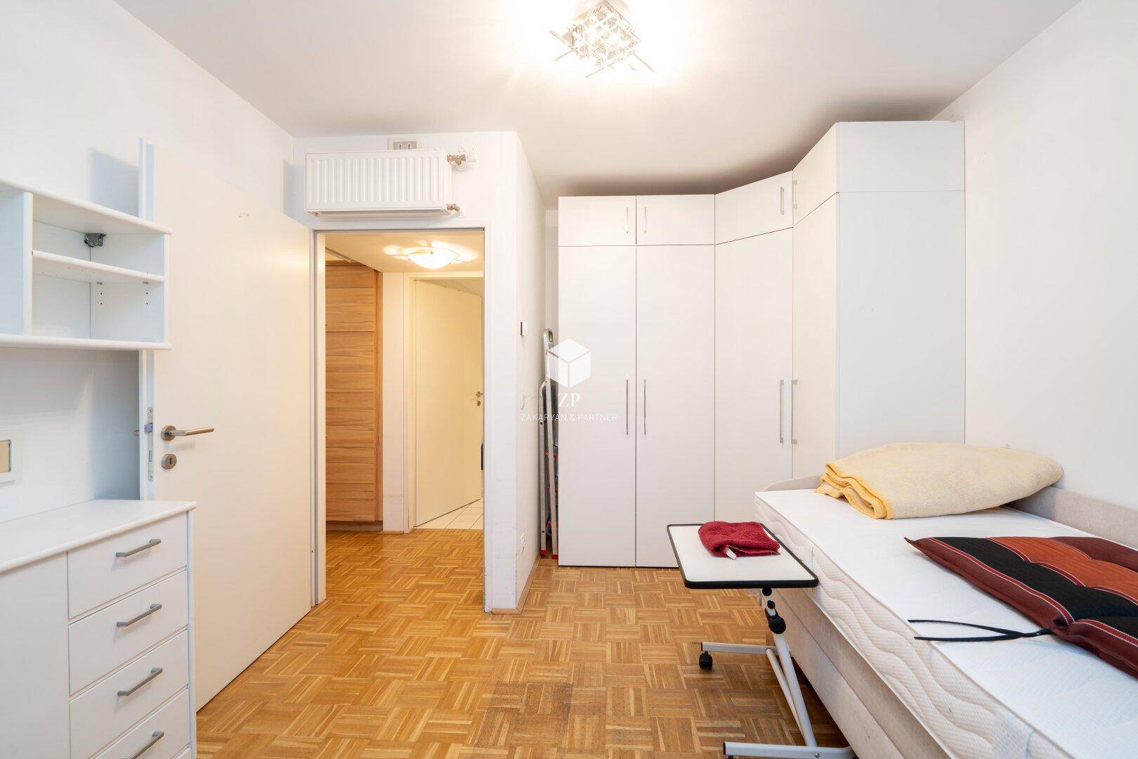 Schlafzimmer mit Einzelbett und großem weißen Eckkleiderschrank.