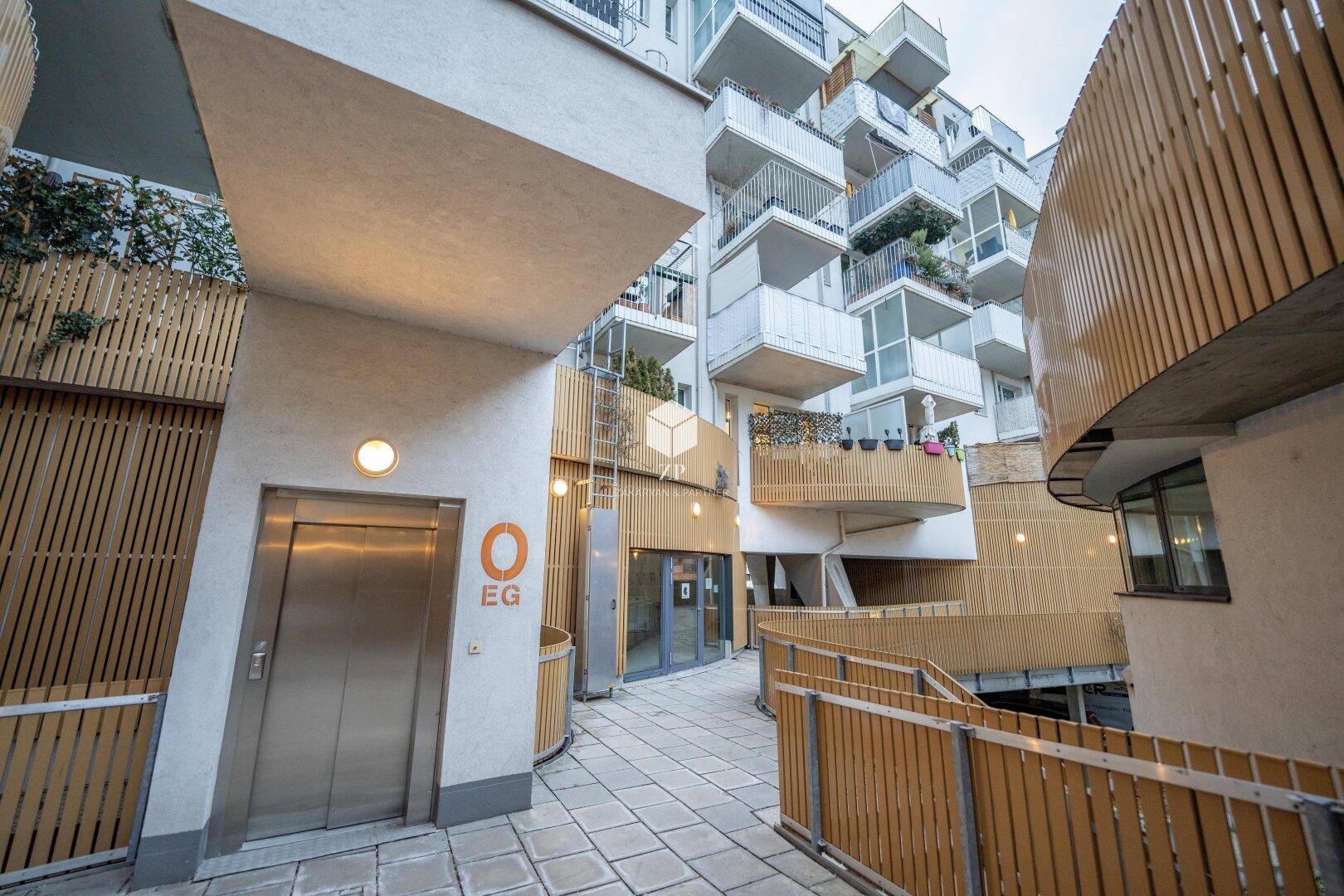 Eingangsbereich eines modernen Wohnkomplexes mit Aufzug und Holzverkleidung.