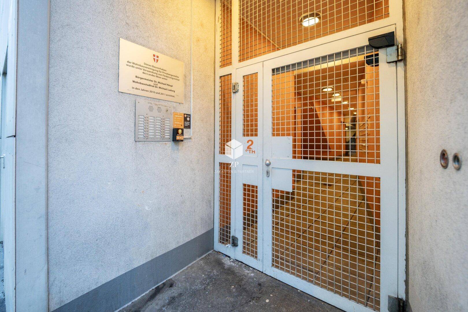Eingangsbereich des Gebäudes mit Gittertür und Klingelanlage.