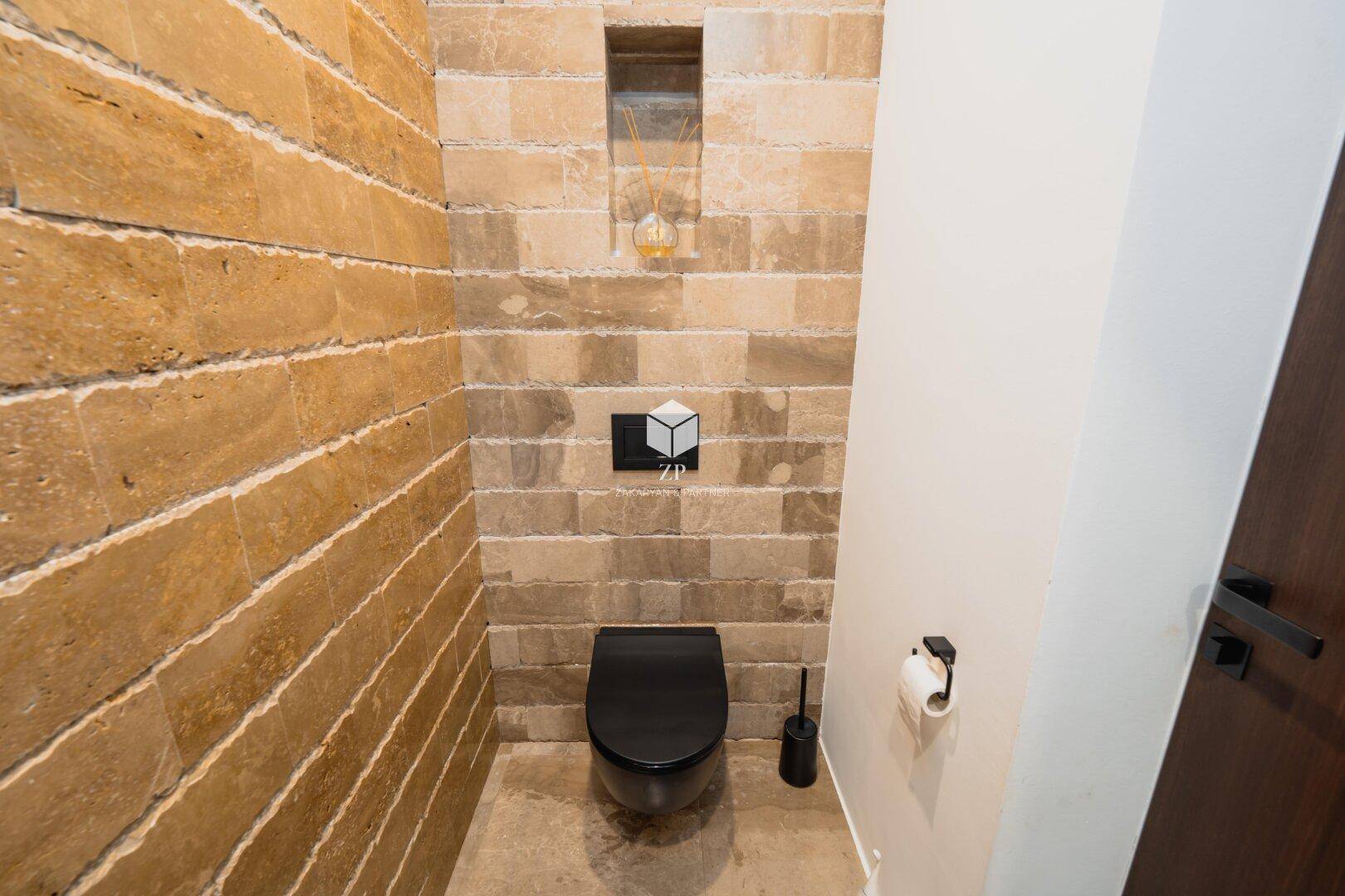 Modernes Gäste-WC mit Natursteinwänden und einer eleganten schwarzen Wandtoilette.