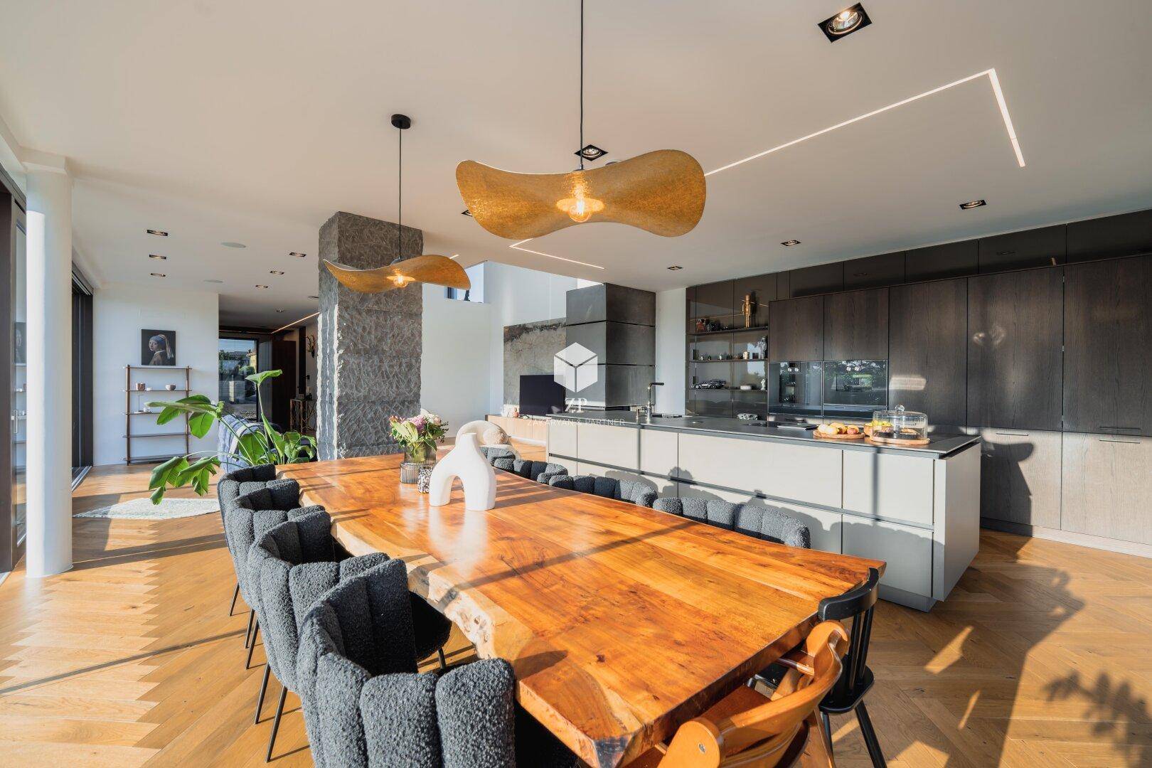 Heller Essbereich mit massivem Holztisch und Designerleuchten, offen zur modernen Küche und mit Weitblick.