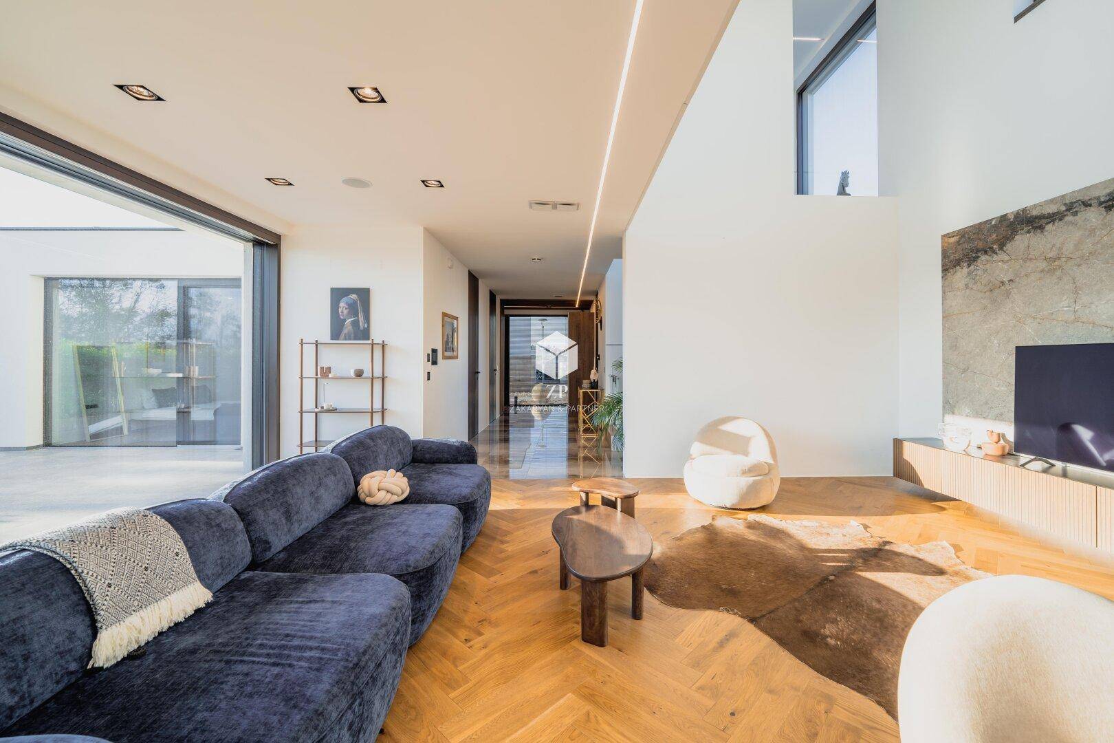 Lichtdurchfluteter Wohnbereich mit blauer Couch, hohen Decken und Blick in den modernen Flur.