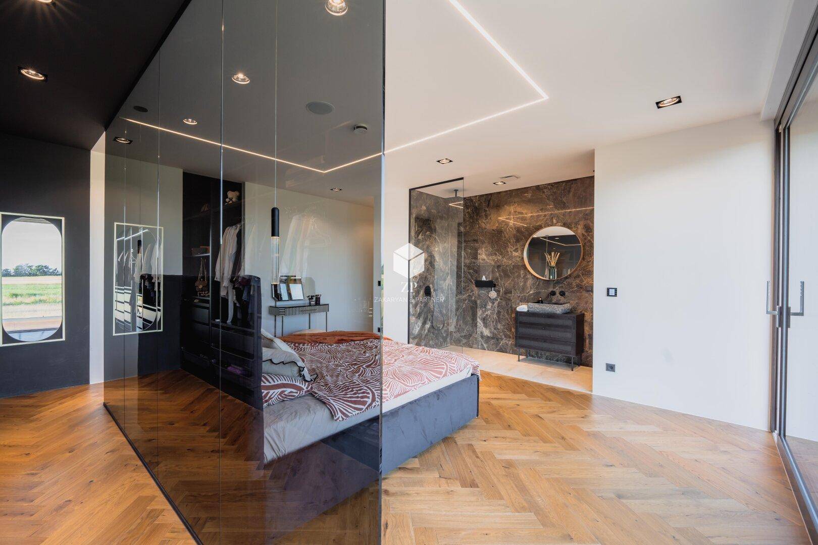 Modernes Schlafzimmer mit Glasabtrennung zum begehbaren Kleiderschrank und offenem Badbereich mit Dusche.