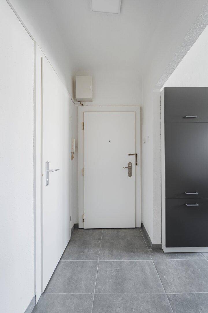 Eingangsbereich mit Fliesenboden, weißer Tür und dunklem Einbauschrank, bietet Stauraum.