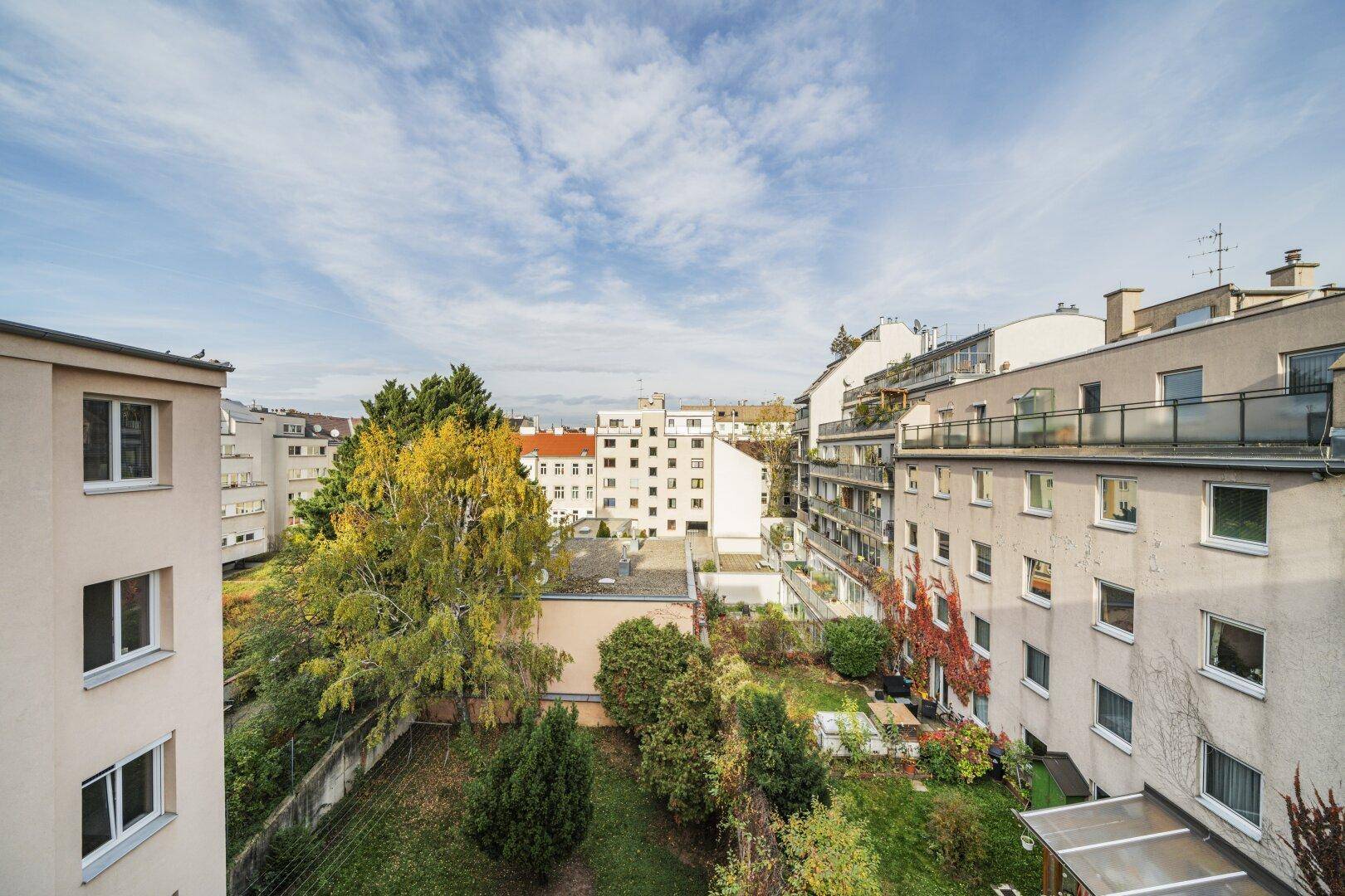 Blick auf den begrünten Innenhof und umliegende Wohngebäude unter blauem Himmel, bietet Ruhe und Grün.