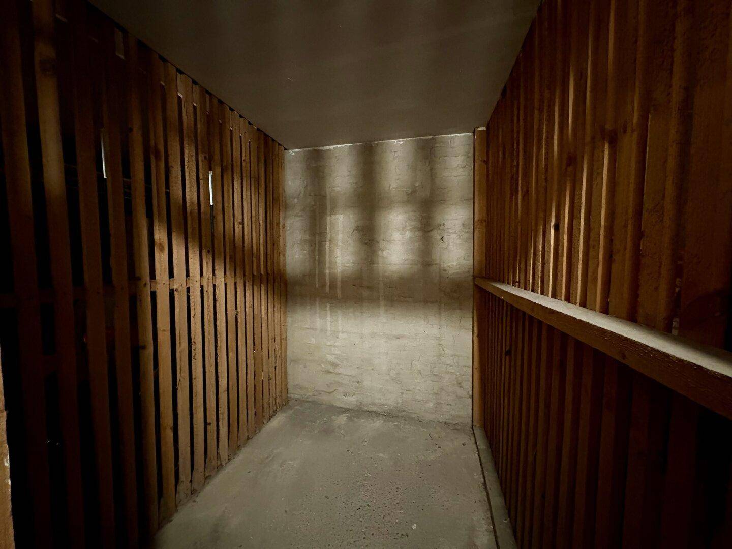 Einfacher Abstellraum mit Holzlattenwänden und Betonboden, ideal für Lagerzwecke.