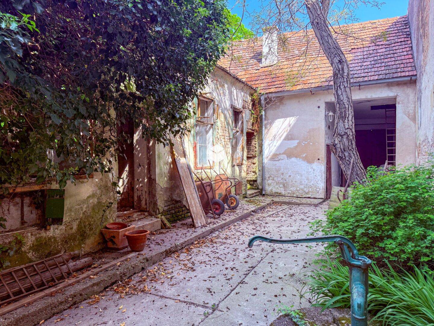 Alter Innenhof mit Kopfsteinpflaster, verwitterten Wänden und einer alten Wasserpumpe.