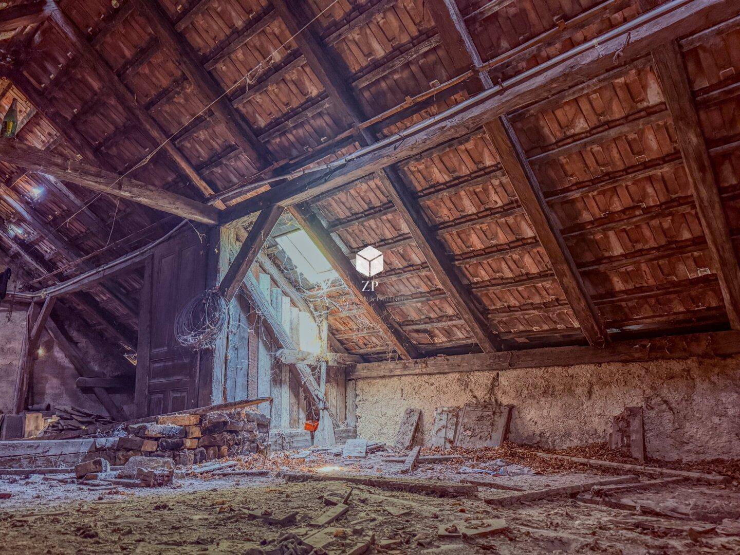 Geräumiger Dachboden mit sichtbaren Holzbalken und Ziegeln, der Renovierung benötigt.