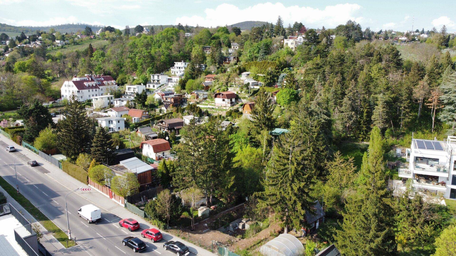 Weitläufige Luftaufnahme einer Wohngegend mit Straßen, Häusern und bewaldeten Hügeln im Hintergrund.