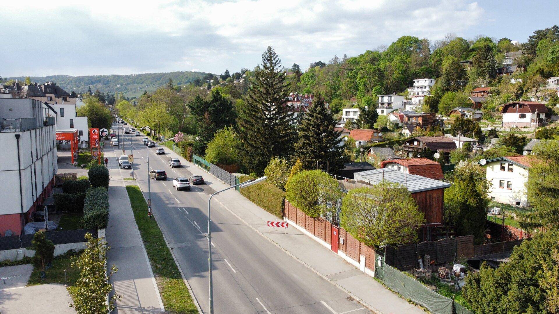 Panoramablick auf eine Wohnsiedlung mit einer Hauptstraße und grünen Hügeln am Horizont.