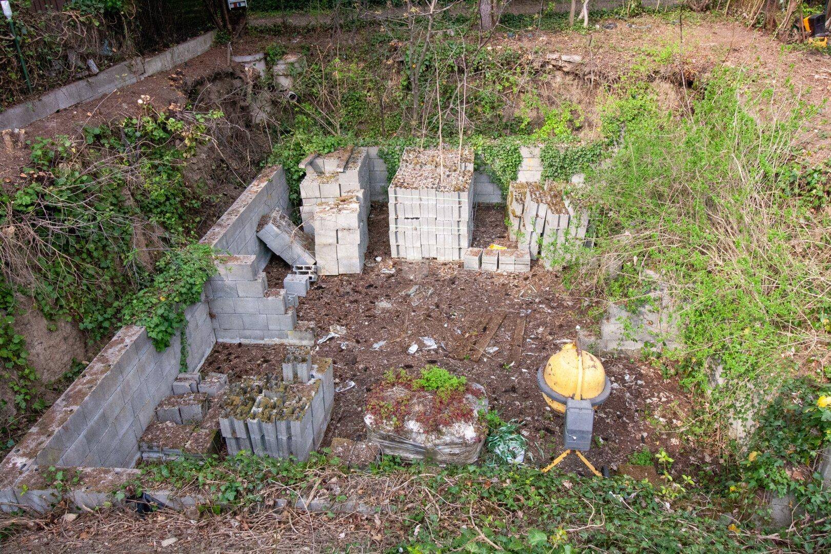 Baustelle auf einem Grundstück mit Betonblöcken, Erdarbeiten und umgebender Vegetation.
