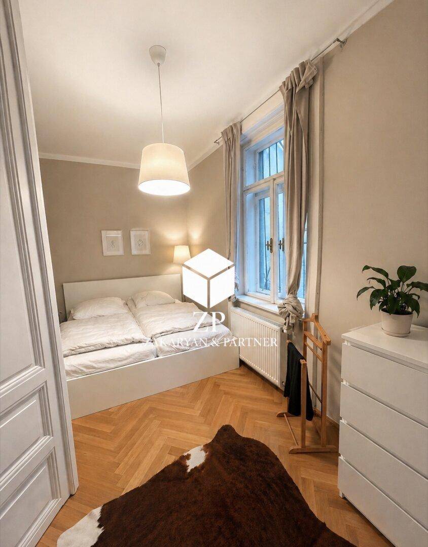 Helles Schlafzimmer mit Doppelbett, Fischgrätparkett und großem Fenster mit Vorhängen.