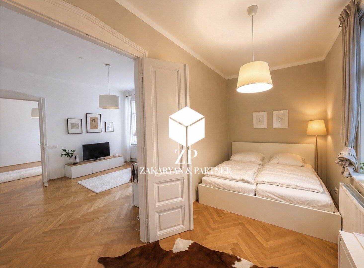 Schlafzimmer mit Fischgrätparkett und offener Verbindung zu einem weiteren Wohnbereich.