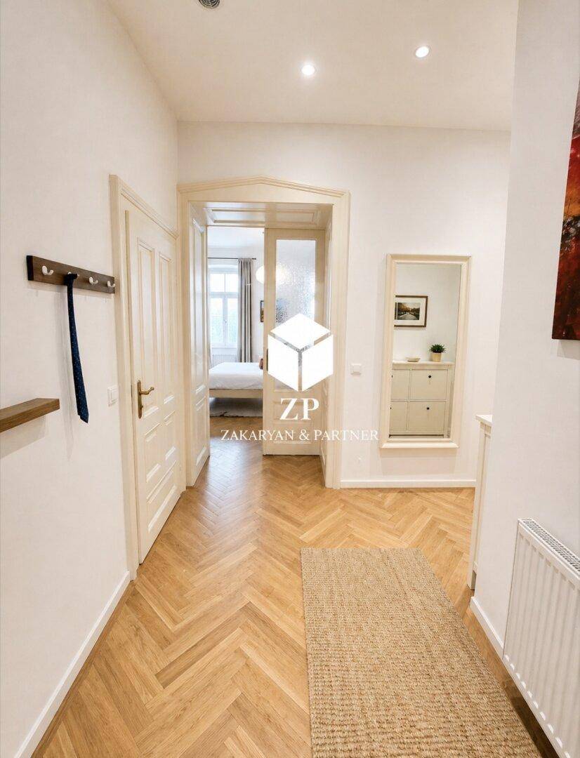Langer Flur mit Fischgrätparkett, Spiegel und Blick in ein angrenzendes Schlafzimmer.