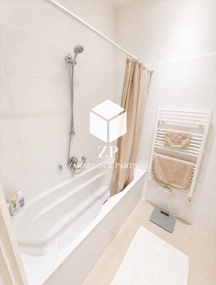 Helles Badezimmer mit Badewanne, Duschvorhang und beheiztem Handtuchhalter.