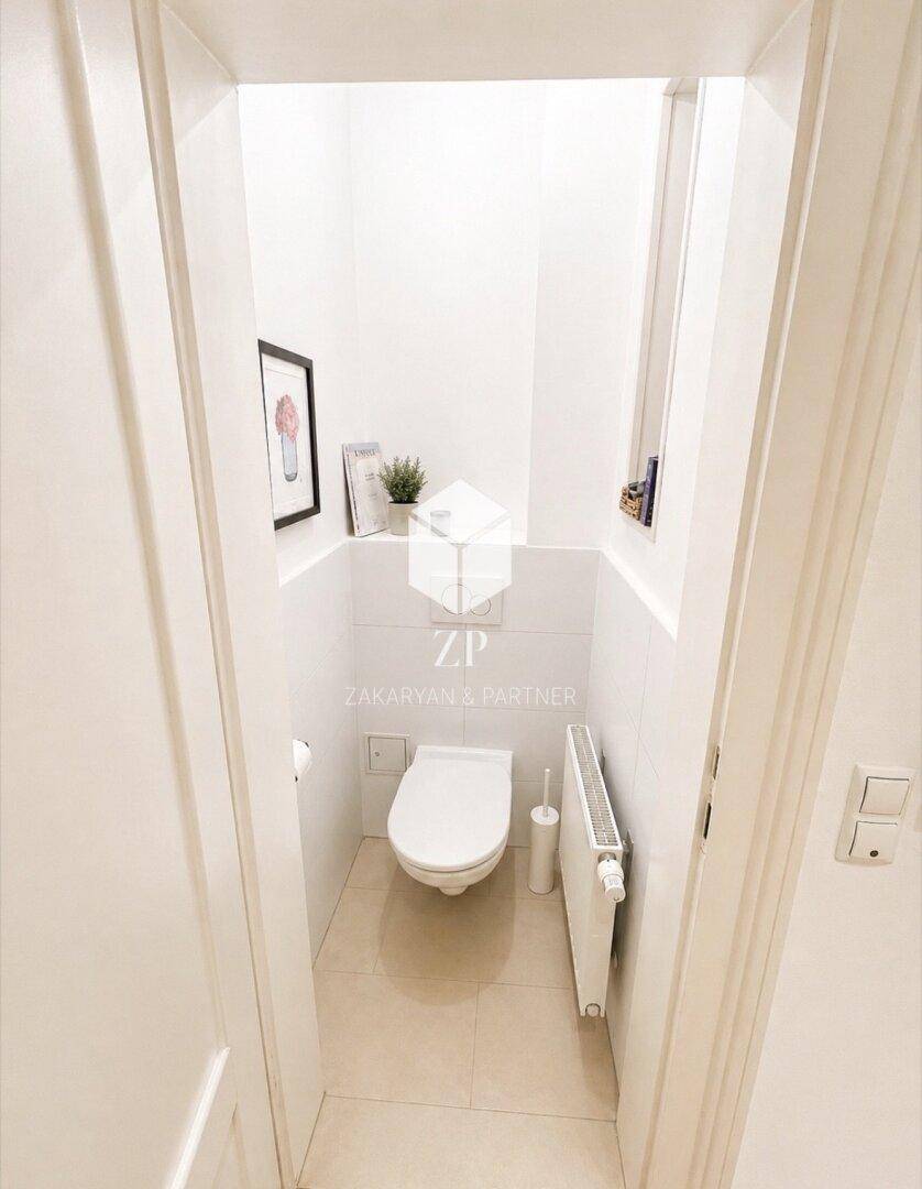 Kleines separates WC mit Wandtoilette und Heizkörper in weiß gefliestem Raum.