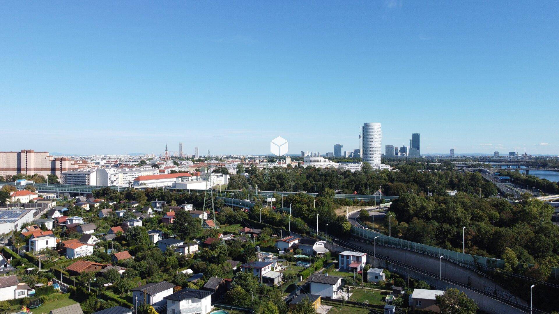 Weitläufige Stadtansicht mit Wohngebäuden, Grünflächen und Hochhäusern am Horizont.