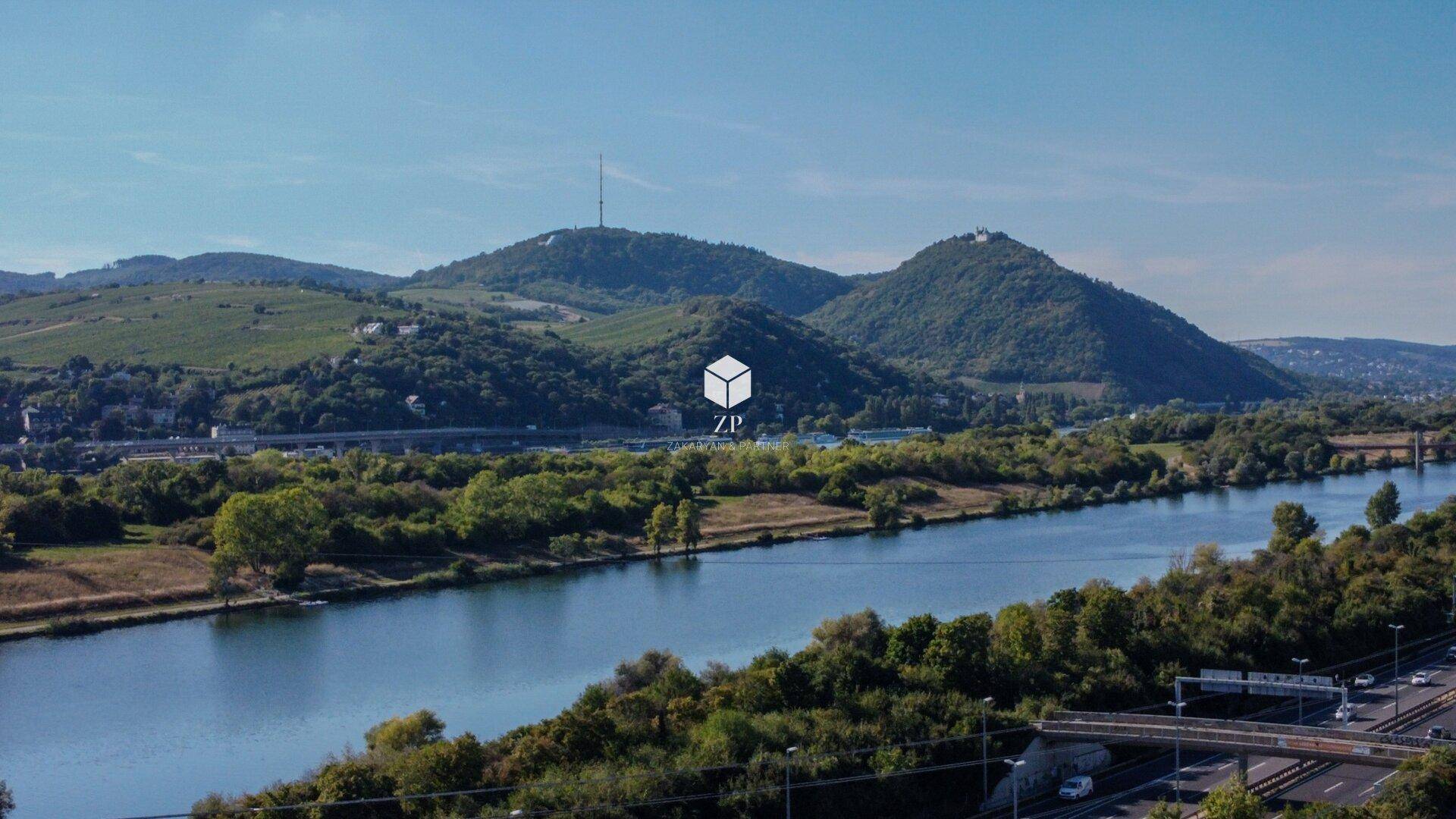 Panoramablick auf einen Fluss, grüne Hügel und eine Autobahnbrücke unter blauem Himmel.