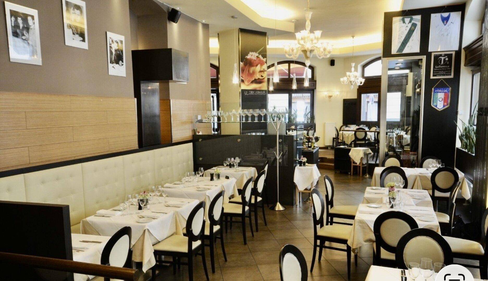 Geräumiger Restaurant-Innenbereich mit vielen gedeckten Tischen, Kronleuchtern und dekorativen Wandbildern.