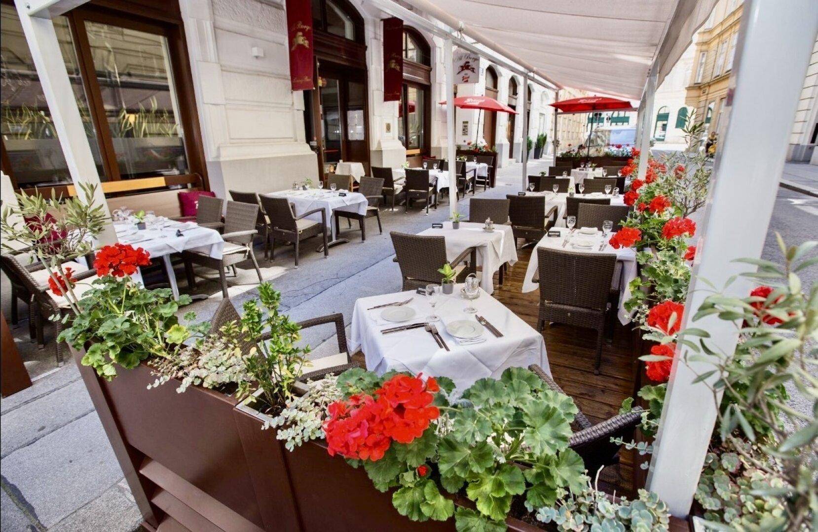 Weitläufige Außenterrasse eines Restaurants mit vielen Tischen, Sonnenschutz und Blumenkästen.