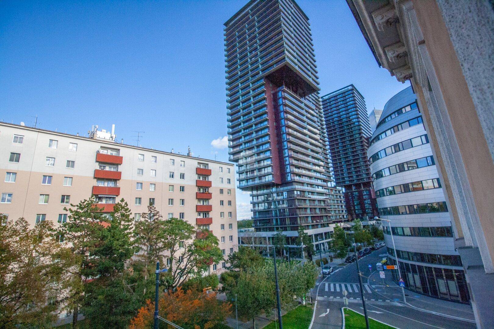 Moderne Hochhäuser und ein älteres Wohngebäude prägen die städtische Skyline mit viel Grün.