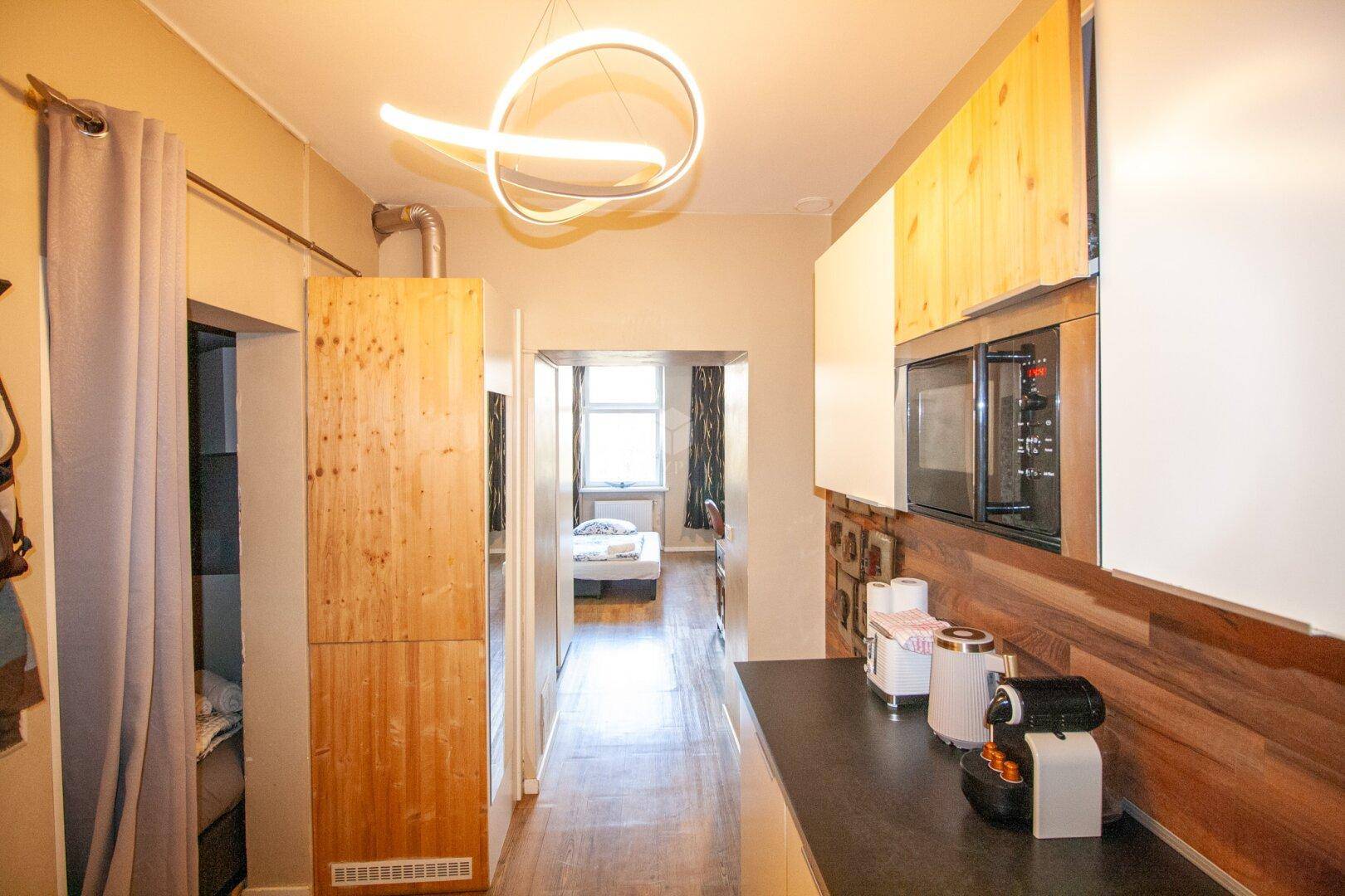 Heller Flur mit Holzakzenten, der zur Küche und einem Schlafzimmer führt, beleuchtet von einer modernen Lampe.