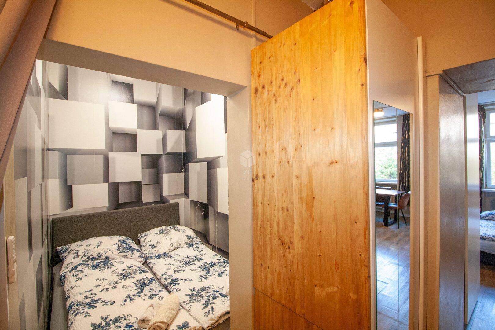 Gemütlicher Schlafbereich mit geometrischer Tapete und einem Doppelbett, abgetrennt durch eine Holzschiebetür.