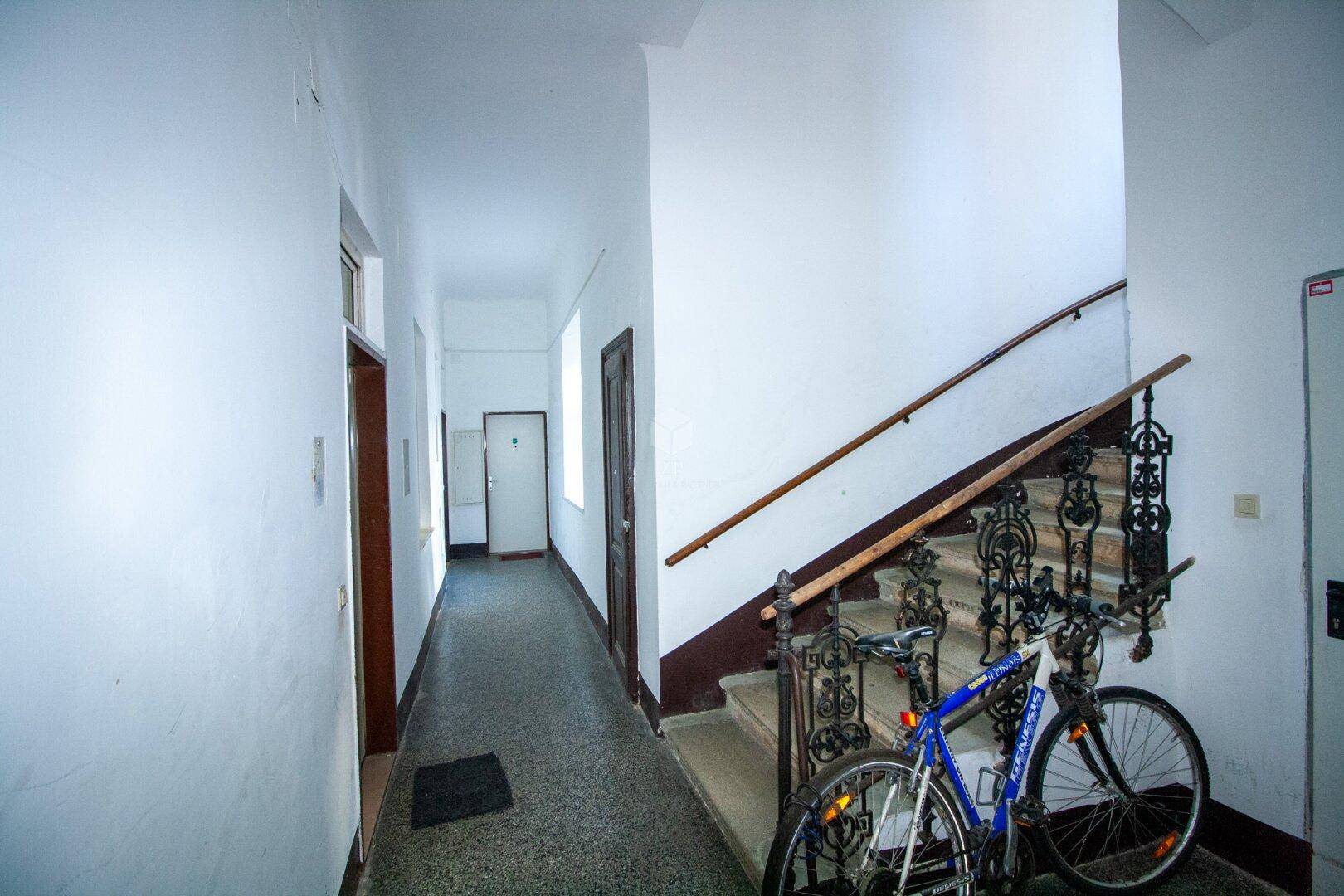 Gemeinschaftlicher Flur und Treppenhaus in einem Altbau mit historischem Geländer und einem abgestellten Fahrrad.