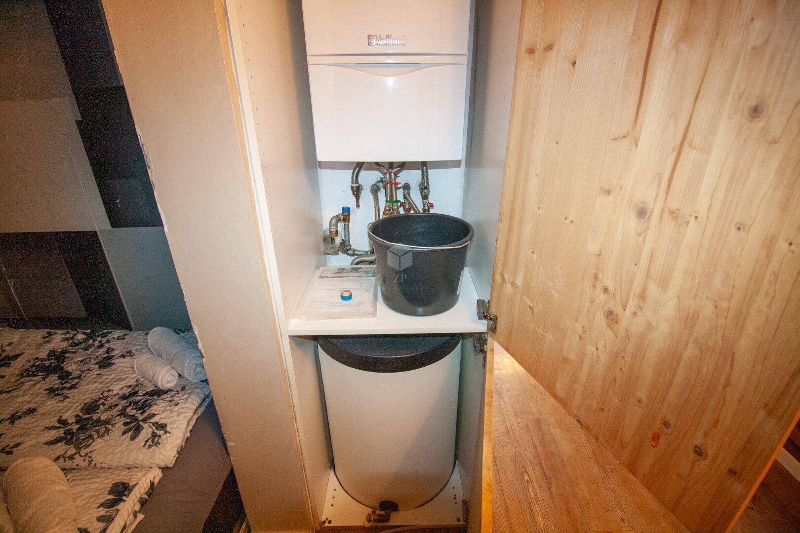 Kleiner Versorgungsschrank mit Warmwasserbereiter und Installationen, neben einem Schlafbereich gelegen.