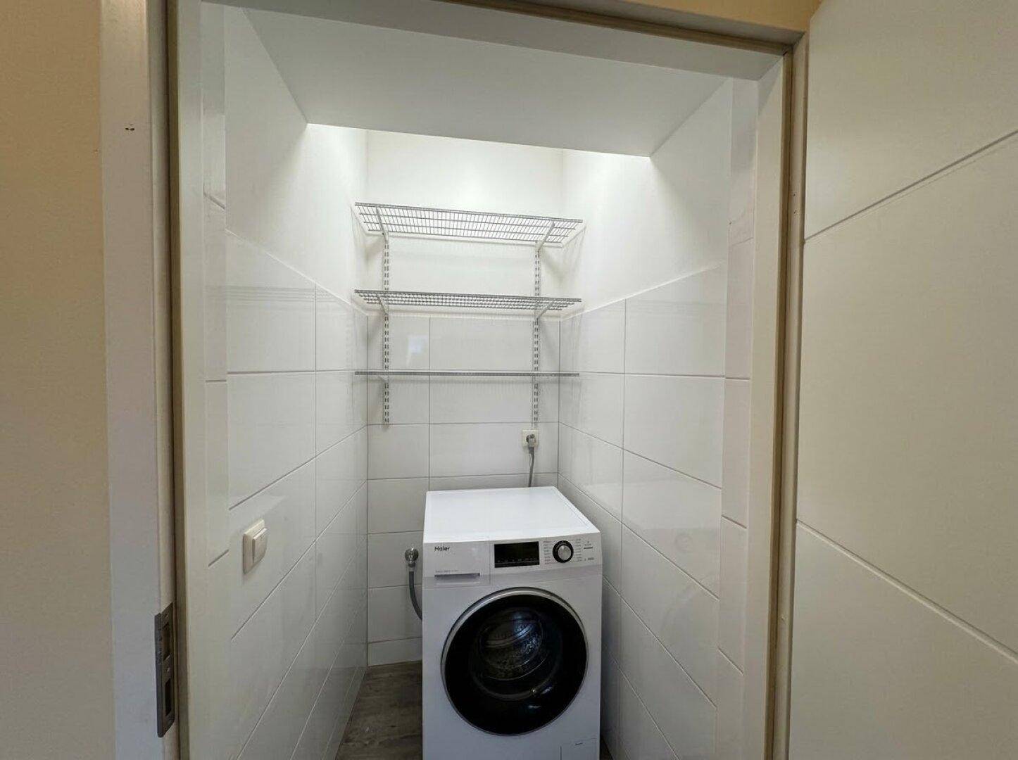 Kleiner Hauswirtschaftsraum mit Waschmaschine und praktischen Regalen, vollständig gefliest.