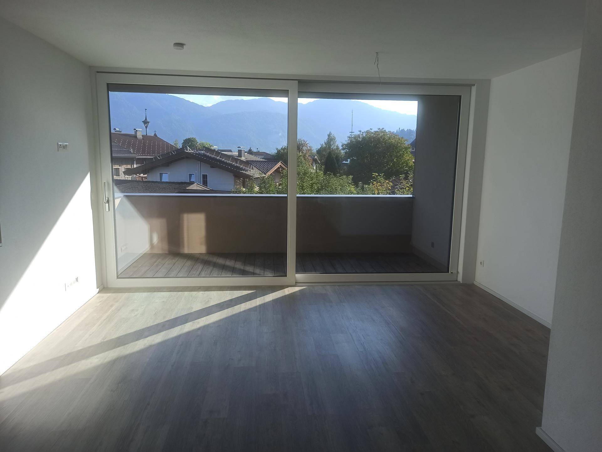 Heller Wohnraum mit großen Schiebetüren zum Balkon und weitem Blick auf die Berge.