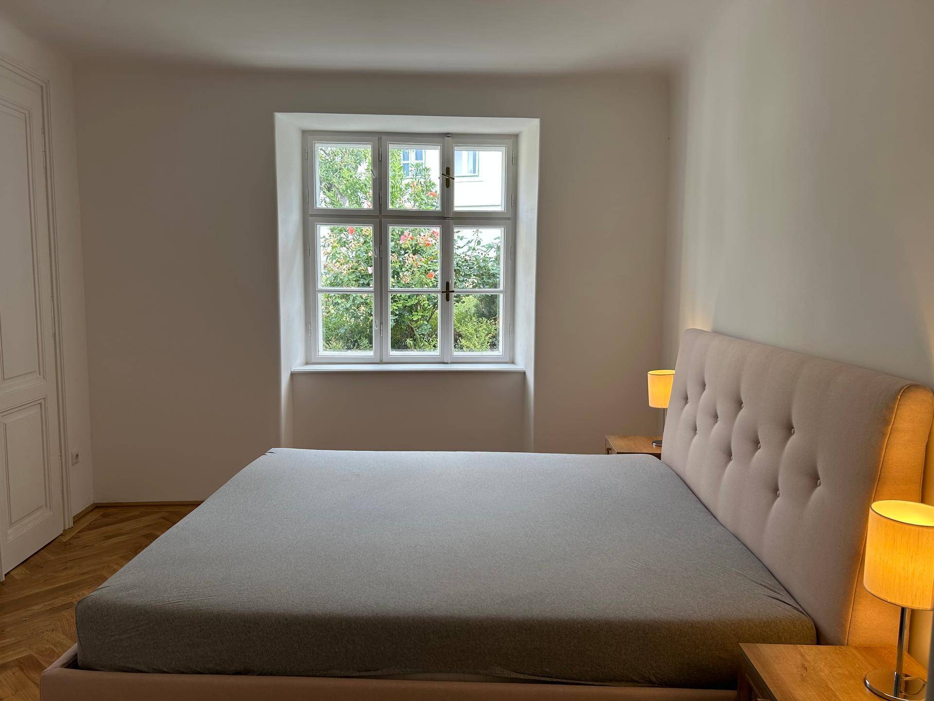 Helles Schlafzimmer mit großem Fenster, Blick ins Grüne und bequemem Doppelbett.