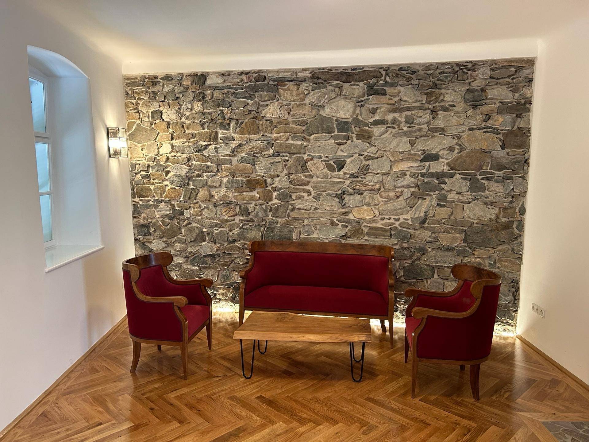 Gemütliches Wohnzimmer mit freigelegter Steinwand, Fischgrätparkett und klassischem roten Mobiliar.