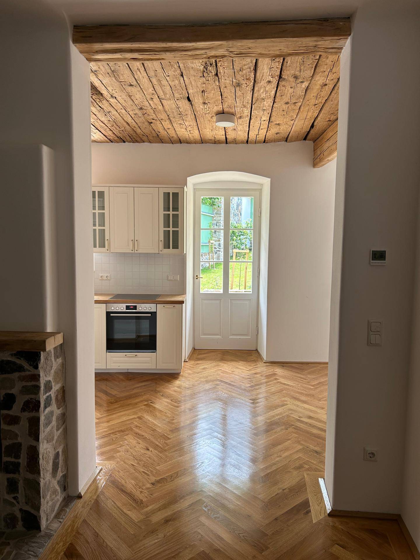 Helle Küche mit Fischgrätparkett, freigelegten Holzbalken an der Decke und Zugang zum Garten.