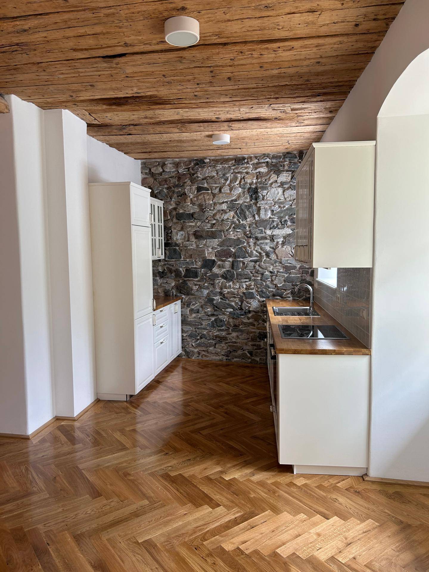 Küche mit rustikaler Steinwand, Holzbalkendecke und modernem Fischgrätparkettboden.