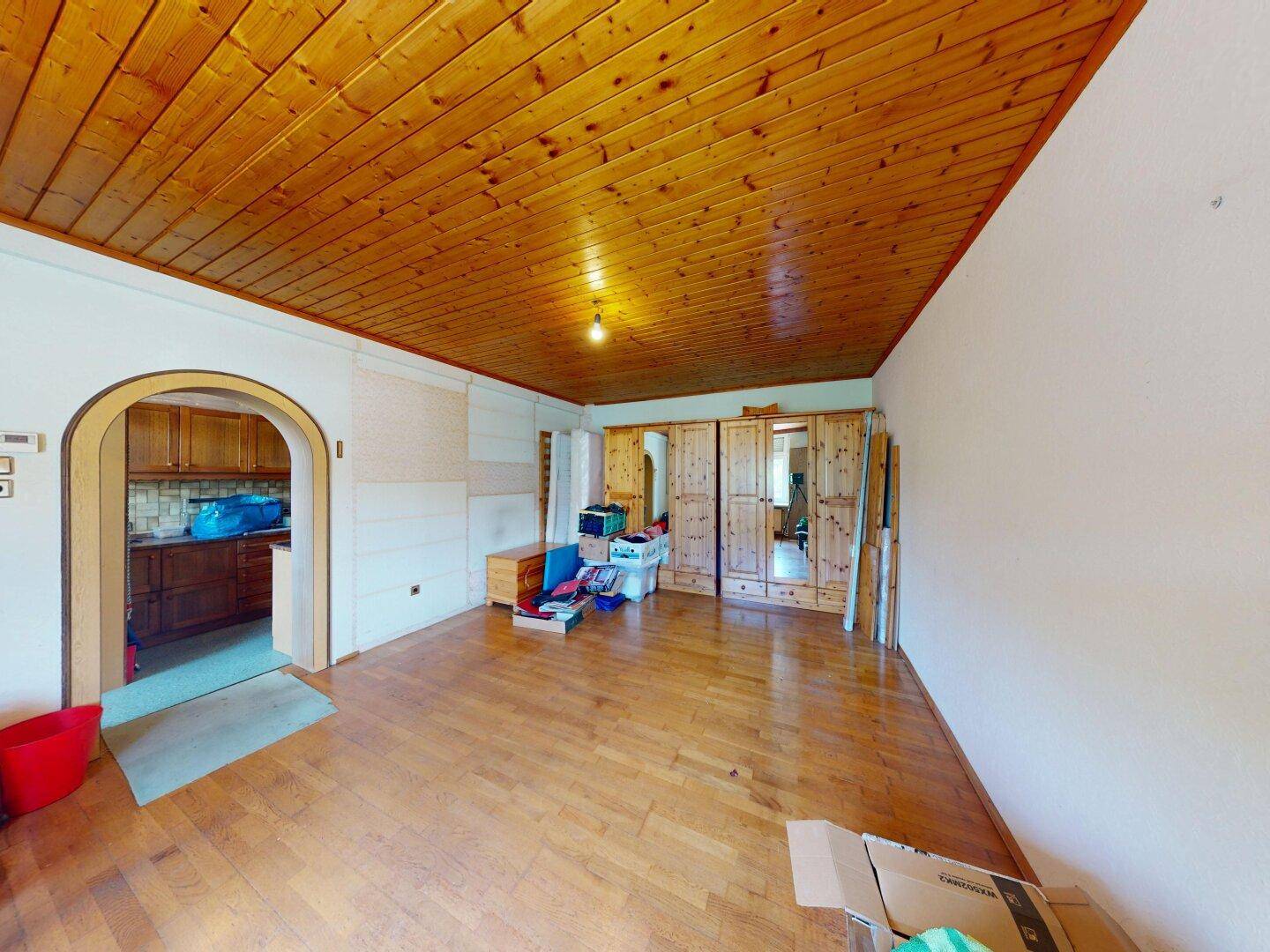 Geräumiger Wohnbereich mit Holzdielenboden, Holzdecke und einem Durchgang zur Küche.