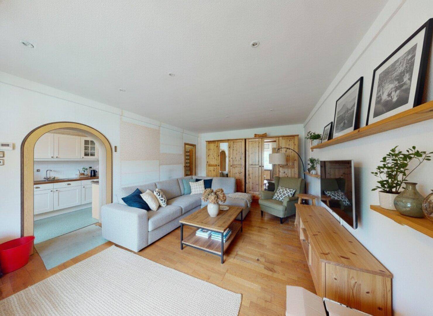 Heller Wohnbereich mit modernem Sofa, Holzboden und Holzdecke, offen zur weißen Küche.